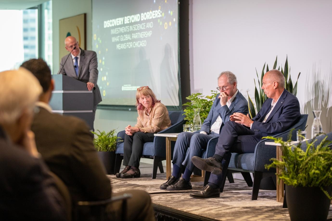 Four people on a stage take part in a discussion before an audience.